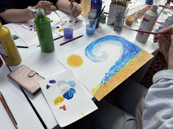 A close-up of some of the art done at the workshop, including a a beach scene with an oil painting of large wave, a beach and the sun.