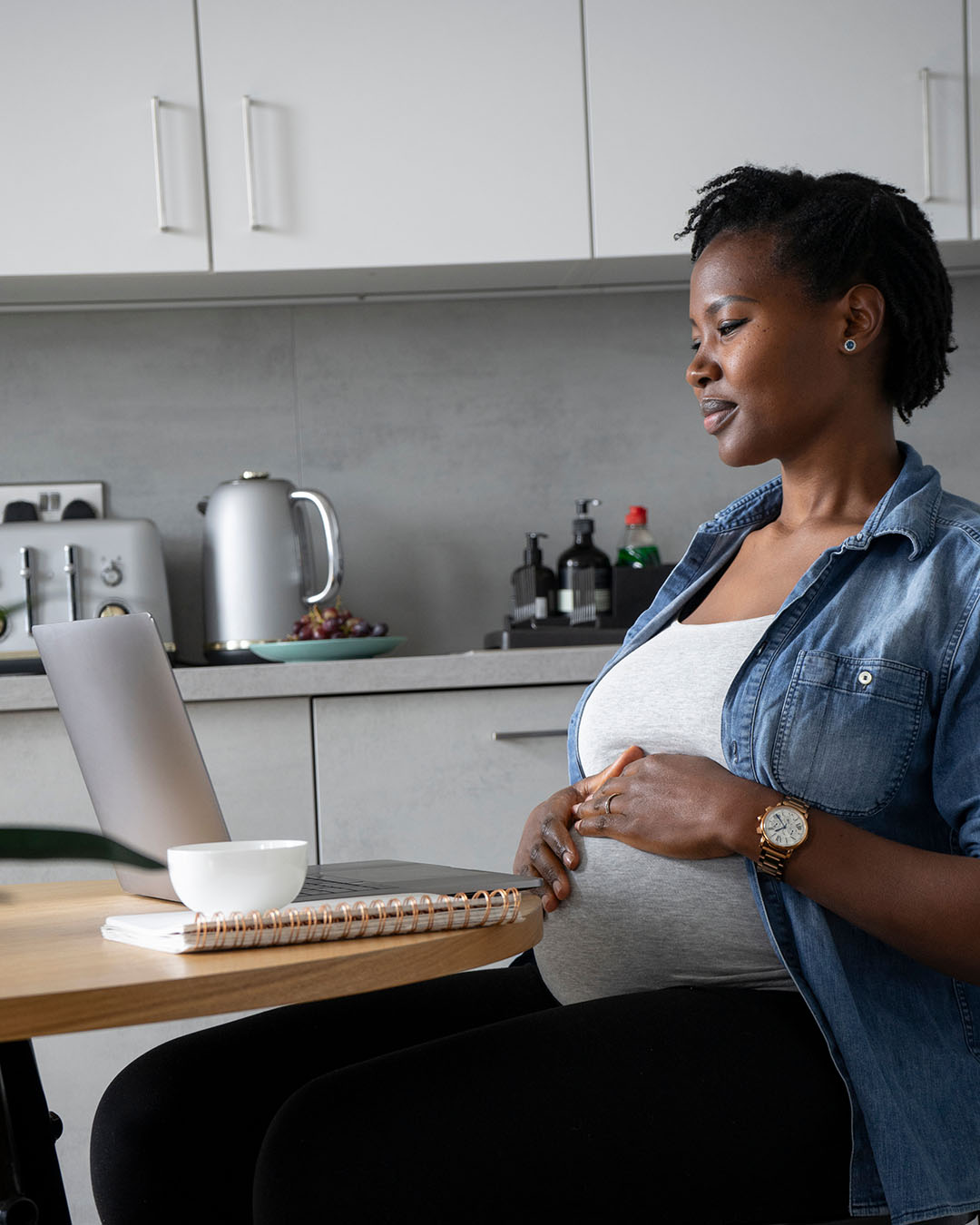 Pregnant woman sat at a table and using laptop in kitchen