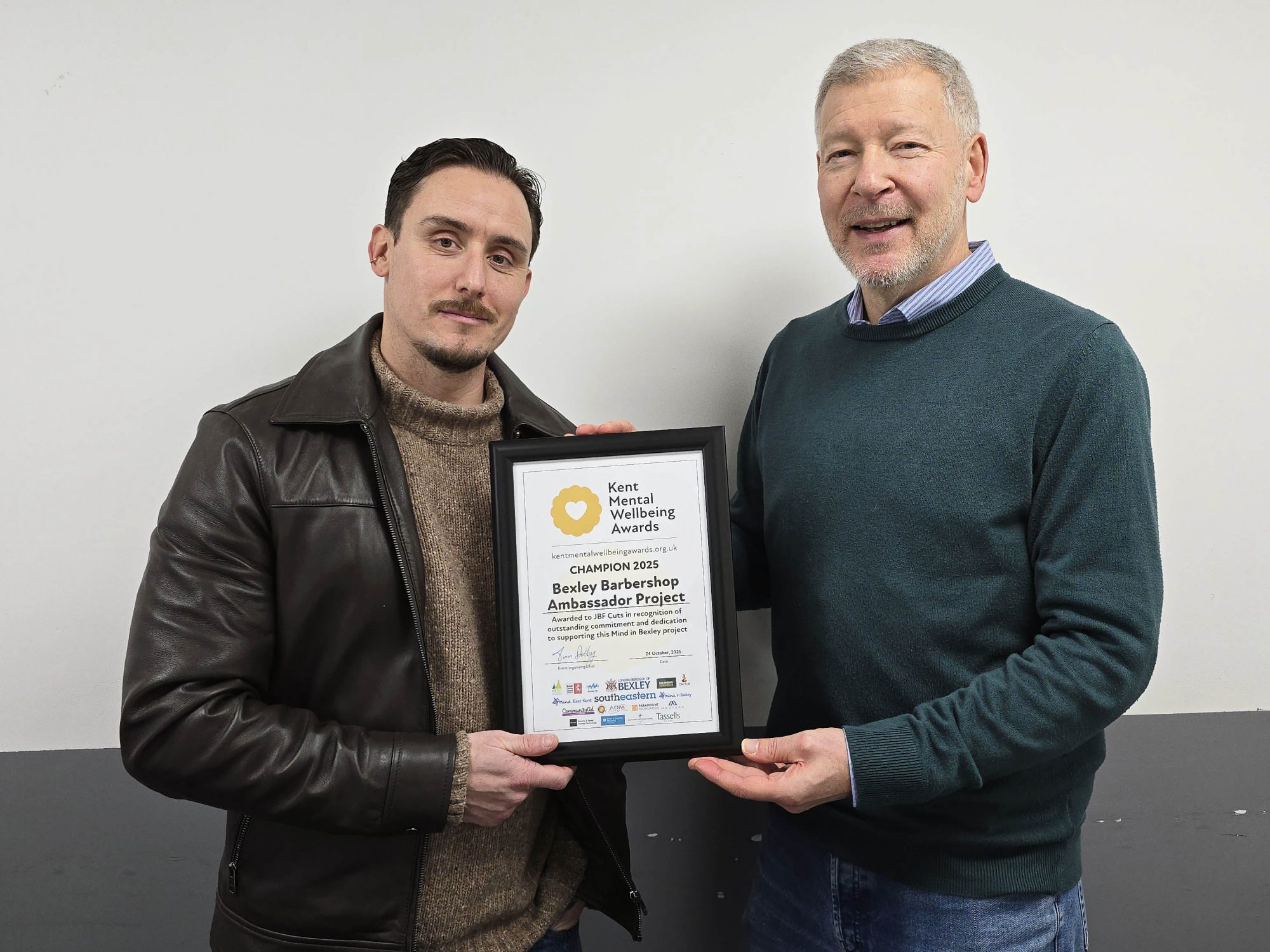 Jon Fortuna is stood smiling and holding his Barbershop Project award certificate, with Mind in Bexley's Development Lead Simon Dolby