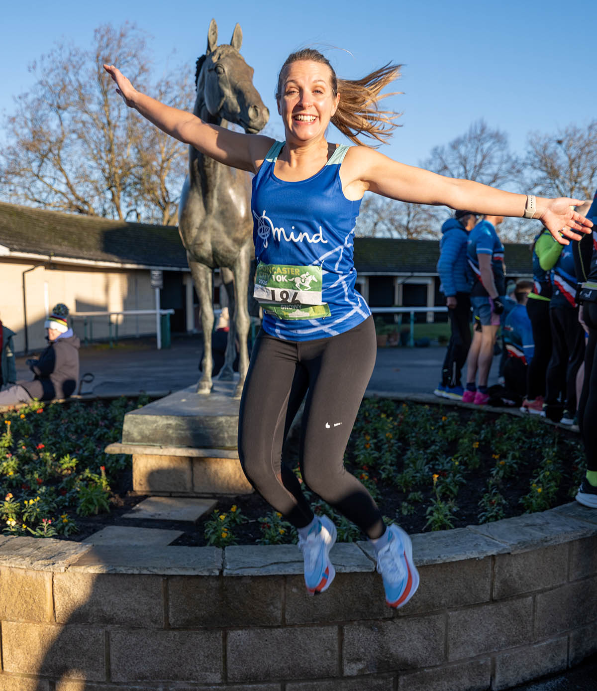 Claire Snowden-Bird jumping for joy after completing a 10k fun run. She's wearing a Mind branded blue running vest