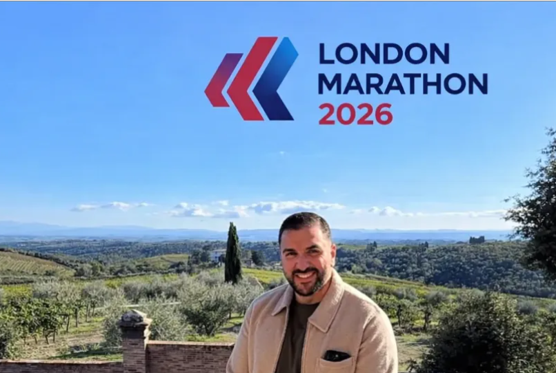 Metin is pictured smiling while he stands outdoors in a rural landscape with rolling green hills, trees and a blue sky in the background. Above him is the words “London Marathon 2026” with the event logo.