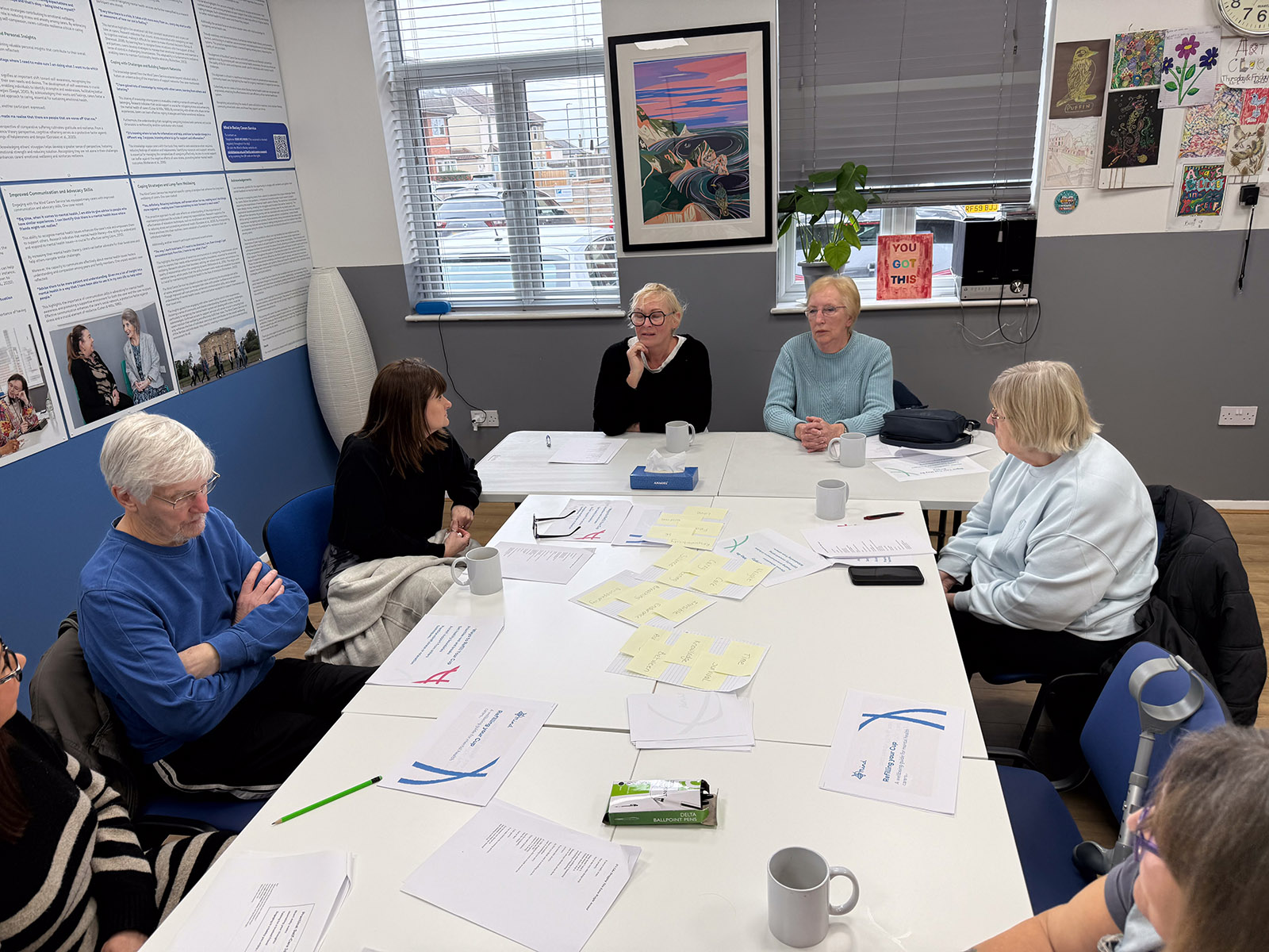 Members of the carers group discussing their poem during a regular meeting at the Mind in Bexley office in Bexleyheath. They are seated at a table that has lots of papers and post-it notes spread across.