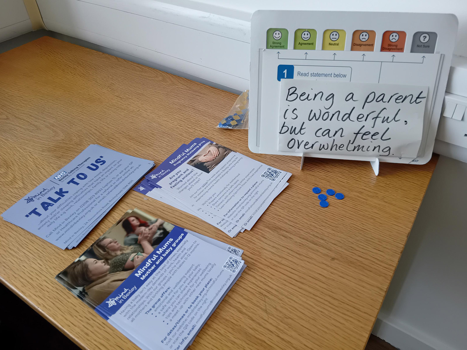Mindful Mums information leaflets and a parenting poll displayed on a table at a family event. The poll statement reads, “Being a parent is wonderful, but can feel overwhelming,” with counters placed to show responses.